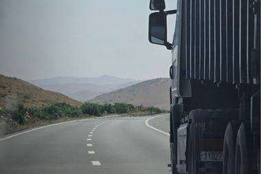 Truck on a winding highway in Douar Ouled El Mesnaoui, Morocco, set in a rocky landscape.